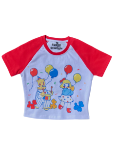 A red and white crop top t-shirt with a graphic print of clowns and balloons on the front, laid plat on a clear background