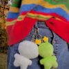 Person wearing a colorful striped sweater with the back of a white plush and a green plush keychains attached to a person's jean skirt.