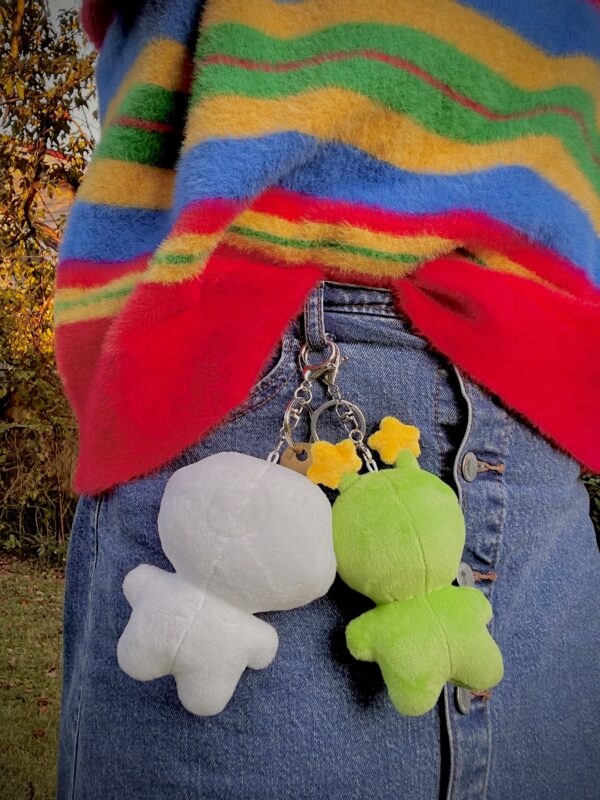 Person wearing a colorful striped sweater with the back of a white plush and a green plush keychains attached to a person's jean skirt.