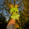 Smiling green alien plush held in front of a tree with a blurred background