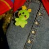 Green Alien plush keychain with a happy face attached to a denim skirt.