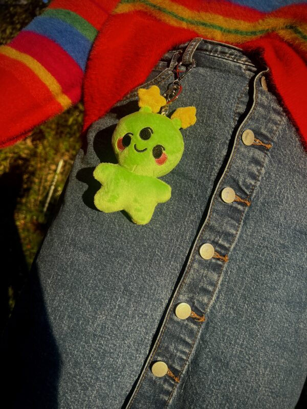 Green Alien plush keychain with a happy face attached to a denim skirt.