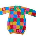 Puzzle Playmat Front Flat lay of the front of the knit sweater dress with a green collar. The design is bright pink, red, yellow, green, and orange puzzle playmat tiles with some tiles having hearts or stars.