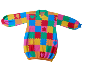 Flat lay of the front of the knit sweater dress with a green collar. The design is bright pink, red, yellow, green, and orange puzzle playmat tiles with some tiles having hearts or stars.