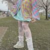 A person wearing a multicolored pastel clown patterned cardigan, paired with a collared blouse and striped skirt, standing outdoors.