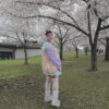 A person wearing a multicolored pastel clown patterned cardigan, paired with a collared blouse and striped skirt, standing outdoors.