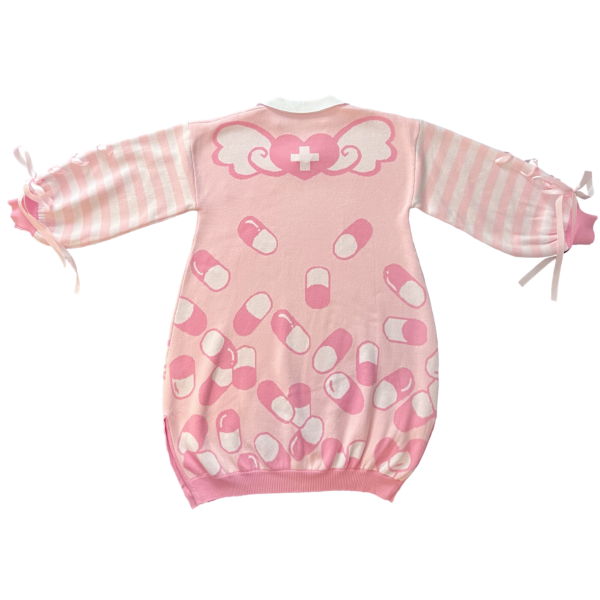 Flat lay image of the back of the pink menhera sweater dress. The sweater dress body is pastel pink with darker pink and white capsules on the bottom with a heart with wings on the top with a white collar. The sleeves are pastel pink and white striped with pastel pink ribbons installed to form a bow on the end of the sleeves.