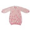 Flat lay image of the front of the pink menhera sweater dress. The sweater dress body is pastel pink with darker pink and white capsules on it. It has a white pointed collar and a removable white ribbon on the center collar. The sleeves are pastel pink and white striped with pastel pink ribbons installed to form a bow on the end of the sleeves. There is a darker pink and white embroidered heart with a cross and wings on the front left chest.