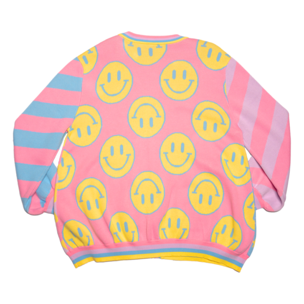Pastel multicolored knit cardigan flayed flat with the back side facing the camera. Cardigan has multicolored stripe sleeves and yellow happy faces on a pink background body panel