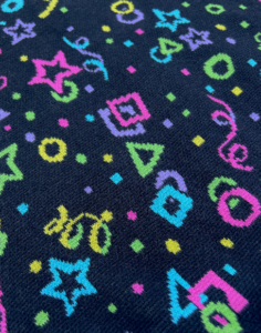 Close up picture of knit bright yellow, pink, purple green and blue stars, circles, squares, and confetti on black background.