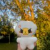 White egg plush with an angry face held in front of a blurred outdoor background with trees.z