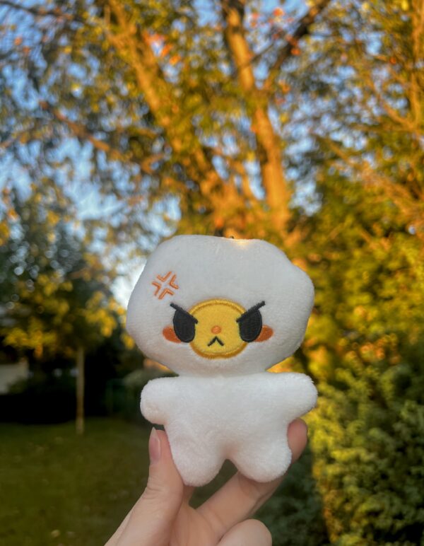 White egg plush with an angry face held in front of a blurred outdoor background with trees.z