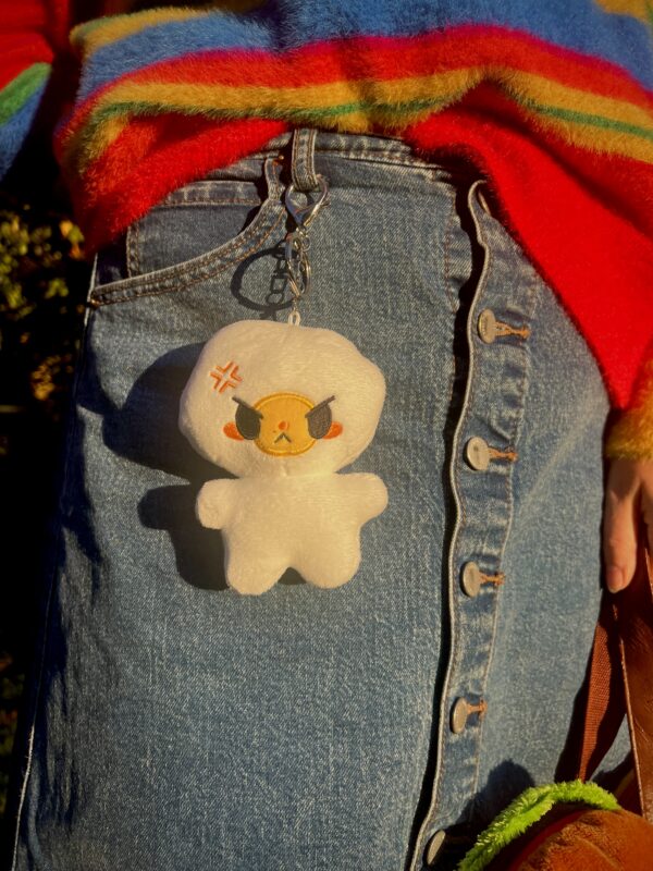 Plush egg keychain with angry expression hanging on a girl wearing a jean skirt and a rainbow sweater