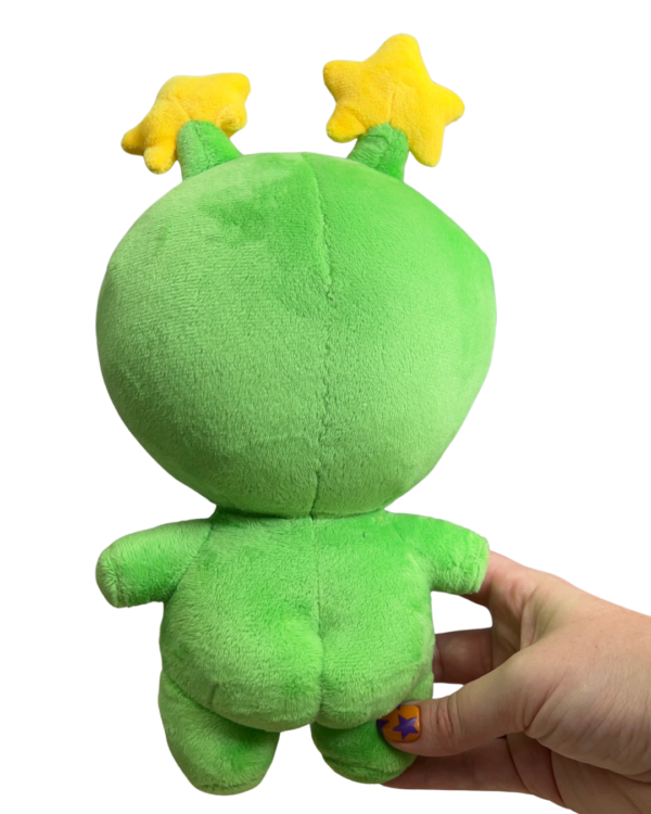 Hand holding a medium plush with its back facing the camera. The Green plush features a round head a small body and two round butt cheeks.