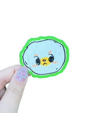 A hand holding a round egg sticker with a character illustration on it on a clear backdrop.