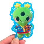 A plush alien sticker with a cartoon character design, held up against a clear background