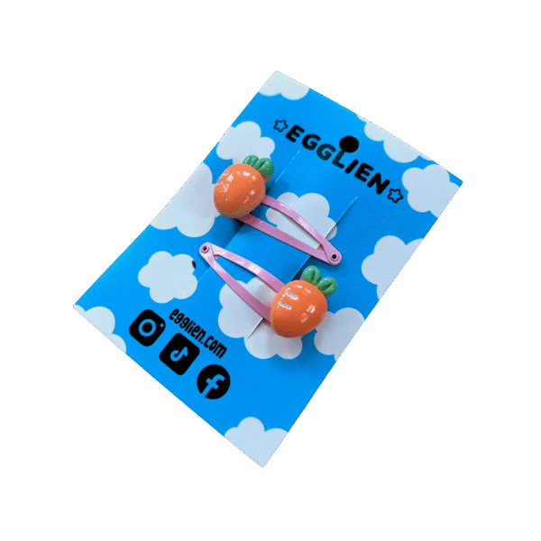 A pair of orange carrot cabochons on pink hairclips both on backing card that reads "Egglien"