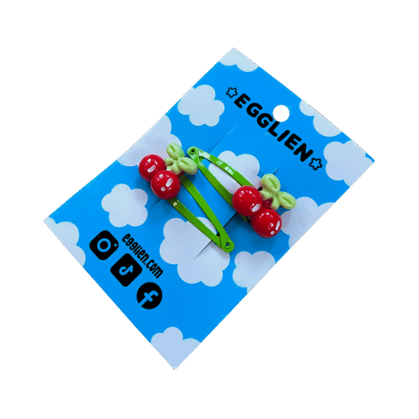 A pair of red cherry cabochons on green hairclips both on backing card that reads "Egglien"