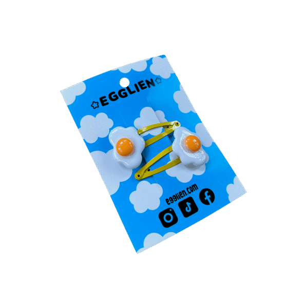 A pair of fried egg cabochons on yellow hairclips both on a blue backing card that reads "Egglien"