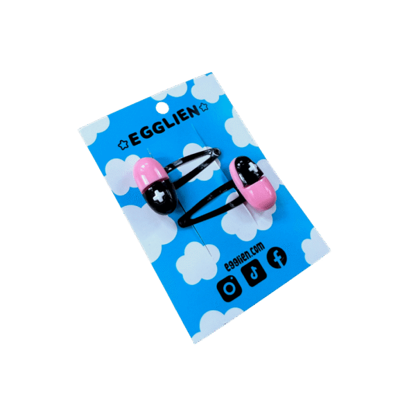 A pair of black and pink capsule cabochons on black hairclips both on blue backing card that reads "Egglien"