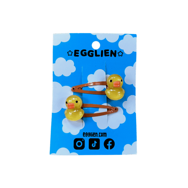 A pair of rubber duck cabochons on orange hairclips both on blue backing card that reads "Egglien"