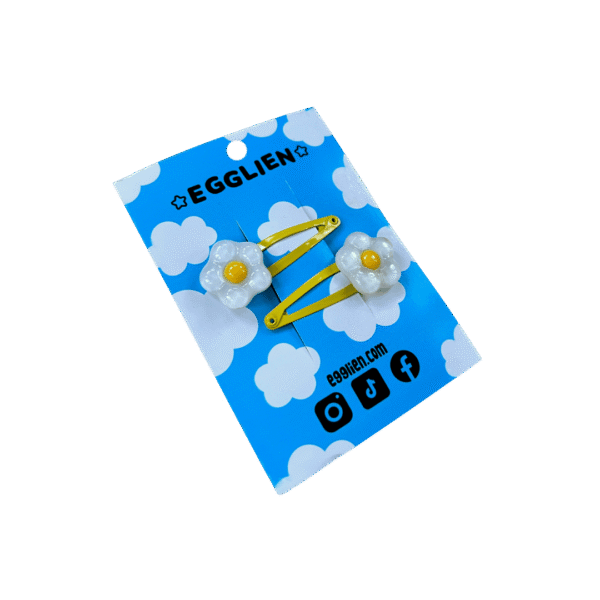 A pair of white and yellow flower resin cabochon on yellow hairclips both on backing card that reads "Egglien"