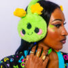 Girl from the shoulders up with her face to the side of the camera showing the alien plush ear muffs shes is wearing. In addition she has chunky green bracelets, a few rinks, and some matching green face gems.