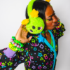 Girl in a 3/4 turn facing slightly away from the camera wearing cheerful green plush alien ear muffs and a roller rink carpet cardigan design.