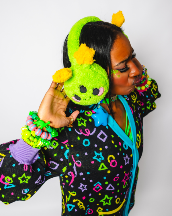 Girl in a 3/4 turn facing slightly away from the camera wearing cheerful green plush alien ear muffs and a roller rink carpet cardigan design.
