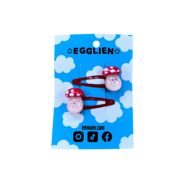 A pair of playful mushroom cabochons on red hairclips both on a blue backing card that reads "Egglien"