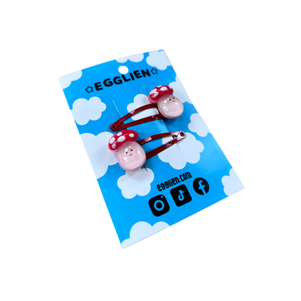 A pair of playful mushroom cabochons on red hairclips both on a blue backing card that reads "Egglien"