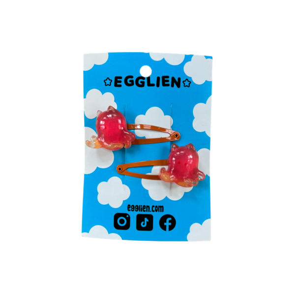 A pair of orangish red cuttlefish cabochons on orange hairclips both on a blue backing card that reads "Egglien"