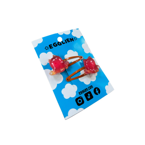 A pair of orangish red cuttlefish cabochons on orange hairclips both on a blue backing card that reads "Egglien"